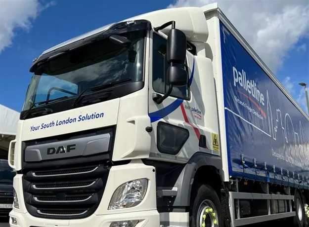 A close-up view of a Palletline Whitehead DAF truck, with “Your South London Solution” branding on the cab and a blue trailer featuring the Palletline logo and London skyline graphic under a partly cloudy sky.